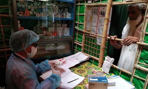 A health worker in protective kit distributes medication to an older man